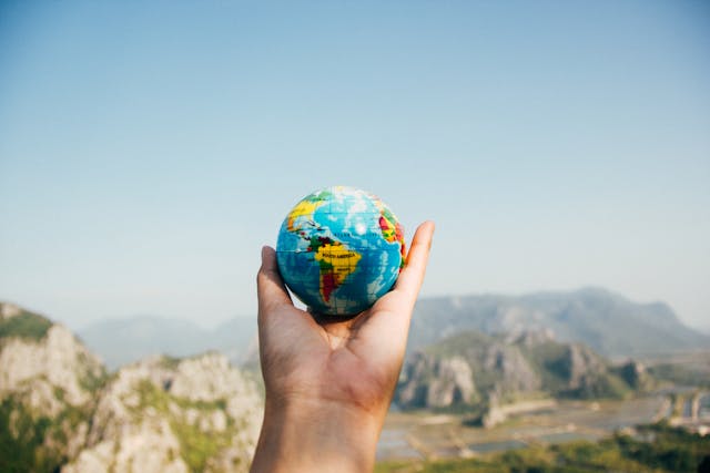 Hand holding a small globe with mountains in the background, representing global connection